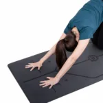 Black yoga mat with alignment guides demonstrated during a forward bend pose, highlighting hand positioning and posture accuracy.